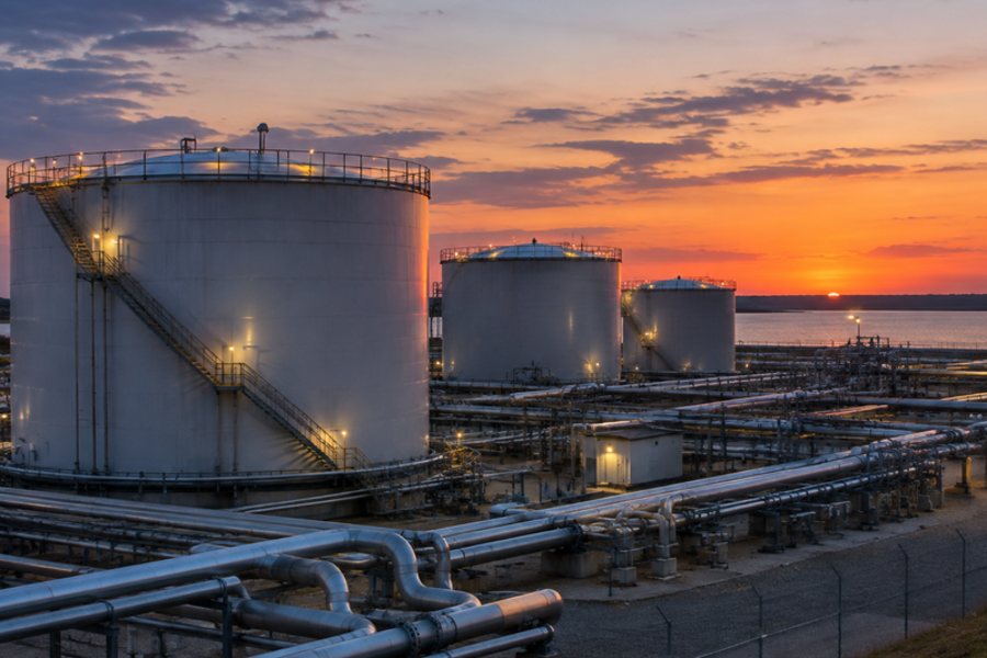 Cylindrical steel storage tanks and pipework at an oil and gas terminal at dusk